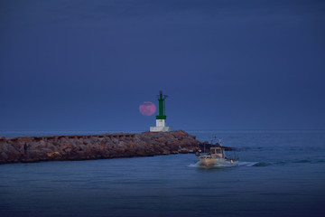 fishing boat entering the mouth of the port with a full moon over the horizon