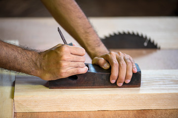 Hands of a carpenter planed wood with carpenter equipment in workshop. Carpenter, craftsman, art, furniture making wood material or timber industry concept