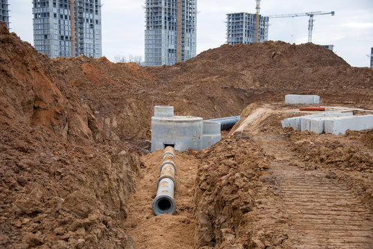 Laying concrete drain pipes and manholes for stormwater system. Connecting a trench drain to a concrete manhole structure at construction site. Construct stormwater and underground utilities,