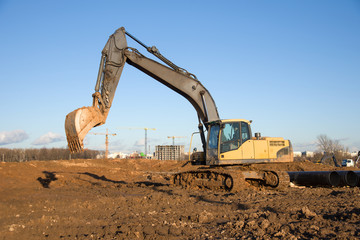 Fototapeta na wymiar Crawler excavator at a construction site during digging ground for laying sewer pipes. Backhoe on earthworks at construction site on blue sky background. Construction machinery for excavation