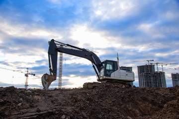 Excavator with bucket at large scale construction site on awesome blue sky background. Backhoe...