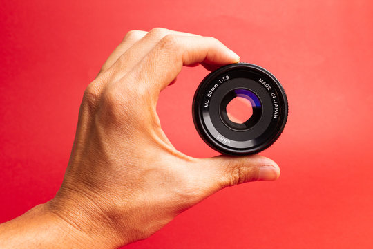 Hand Holding An Old Camera Lens On Red Background