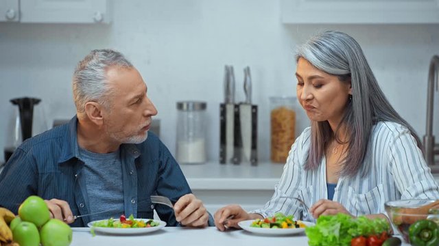 senior interracial couple eating salad in kitchen