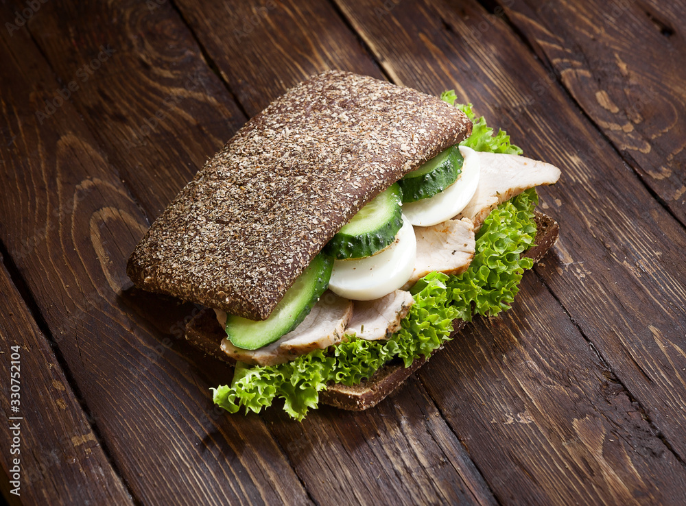 Wall mural turkey sandwich with dark bread, fresh green salad, eggs and cucumbers on rustic wooden table surfac