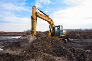 Obraz premium Excavator during earthmoving work at open-pit mining on blue sky background. Loader machine with bucket in sand quarry. Backhoe digging the ground for the foundation and for laying sewer pipes