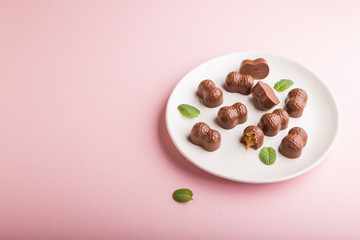 Chocolate caramel candies on a pastel pink background. Side view, copy space