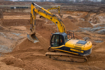 Excavators at earthworks on construction site. Backhoe loader digs a pit for the construction of the road. Digging trench for laying sewer pipes drainage in ground. Earth-Moving Heavy Equipment