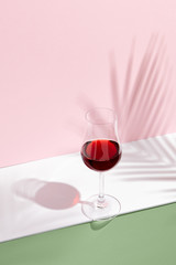 Red wine on creative background. Shadows of palm leaf on pink walls