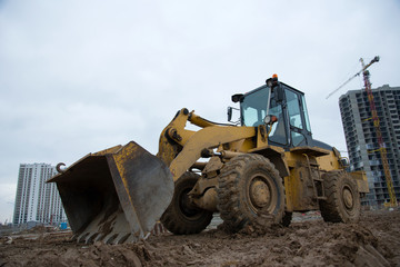 Front-end loader working at construction site. Earth-moving heavy equipment for road work. Public works, civil engineering, road building. Construction machinery for loading, lifting cargo