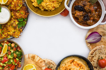 Frame of Israeli food: esik fleisch - beef stew with damson plums and spices, hummus,  potato latkes, ptitim, pita bread, israeli salad. Grey background.
