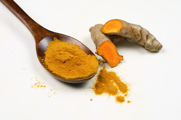Turmeric powder in a wooden spoon and fresh turmeric roots isolated on a white background is an ingredient in turmeric foods and ingredients in skin care products. Turmeric helps the skin to be strong