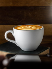 cup of latte art cappuccino coffee with steam on black background and antique books