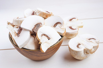 Sliced raw chapminons in and around a wooden bowl on a white wooden background. The concept of healthy food, vegetarianism, mushrooms.