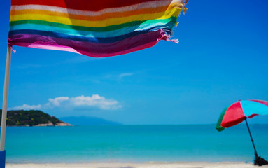 LGBT rainbow flag on the beach.  Blue water wite sand.