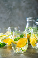 Summer healthy lemonade, cocktails of citrus infused water or mojitos, with lime lemon orange, ice and mint, diet detox beverages, in glasses on gray background.