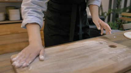 Girl in a black apron kneads the dough on a wooden cutting board close up