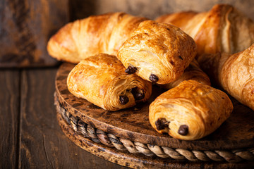 Freshly baked sweet buns puff pastry with chocolate and croissants on old wooden background....