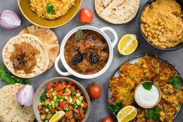 Israeli food: esik fleisch - beef stew with damson plums, hummus,  pita, potato latkes, ptitim,  israeli salad. Grey background.