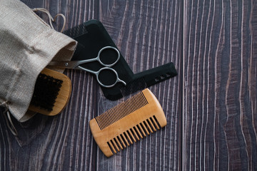 Bag with tools for beard grooming: scissors, brush and combs on wooden background. Top view. Flat lay. Copy space.