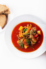 Hot beef hungarian  goulash soup with paprika, beef, potatoes, carrots, onion, pepper and herbs. White background. High key. Top view.