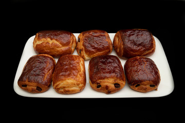  Set of chocolate rolls arranged on a white plate, all on a black background