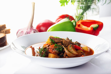 Hot beef hungarian  goulash soup with paprika, beef, potatoes, carrots, onion, pepper and herbs. Ingredients for dish.  White background. High key.