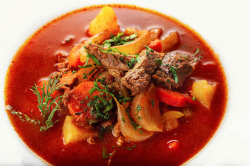 Hot beef hungarian  goulash soup with paprika, beef, potatoes, carrots, onion, pepper and herbs. White background. High key.