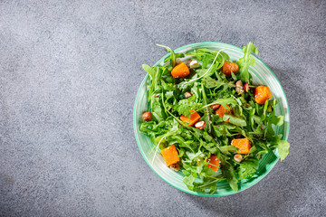 Delicious salad with arugula, baked pumpkin, hazelnut and sesame seeds on green plate. Paleo diet food concept. Top view.