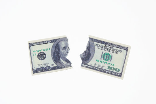 a hundred dollar bill torn in two halves on a white background top view