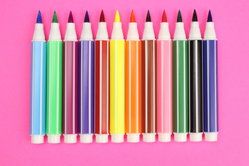 colored markers in a row on a pink background