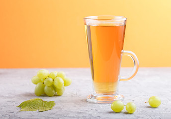 Glass of green grape juice on a gray and orange background. Side view, close up.