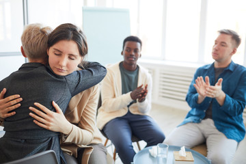 Portrait of young woman embracing female psychologist during therapy session in support group, copy space