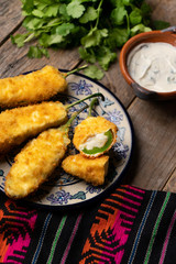 Mexican jalapeno poppers stuffed with cheese and breaded on wooden background