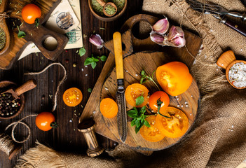 overhead shot of ripe juicy yellow tomatoes and basil on wooden boards with vintage knife on rustic table with spices, herbs, pepper, salt, garlic, sackcloth, food background process of cooking