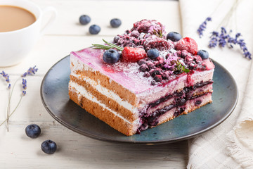 Berry cake with milk cream and blueberry jam on blue ceramic plate with cup of coffee and fresh blueberries on a white wooden background. side view, selective focus.