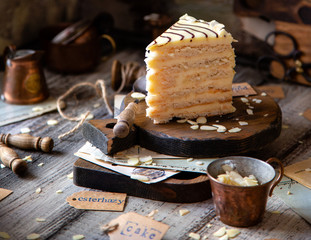 traditional hungarian slice of esterhazy cake on wooden boards on grey wooden table with copper cups, vintage forks, almond flakes opposite concrete wall