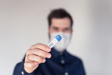 Men during epidemic in medical mask with body thermometer