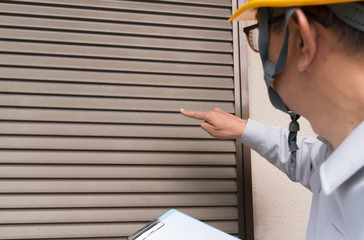 老朽化した住宅　シャッター雨戸を調査するビジネスマン