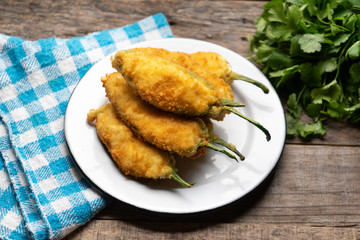 Mexican jalapeno poppers stuffed with cheese and breaded on wooden background