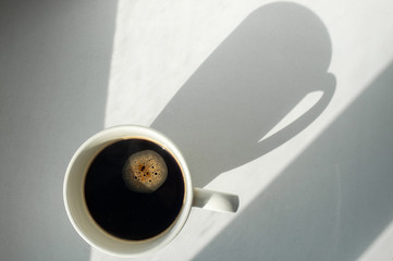 White cup of black coffee on table top view, morning shadow