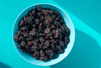 Dry prunes in plate on aqua background, top view