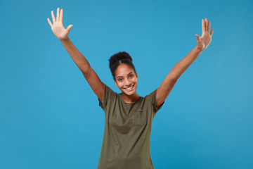 Funny young african american woman girl in casual t-shirt posing isolated on blue background studio portrait. People sincere emotions lifestyle concept. Mock up copy space. Rising spreading hands.