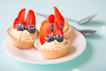 Cakes with fresh berries. Cream tartlet with strawberries and blueberries