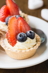 Cakes with fresh berries. Cream tartlet with strawberries and blueberries