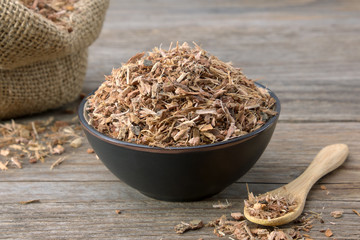 Healthy oak bark in black ceramic bowl  and sack of dry oak bark on background. Herbal medicine.