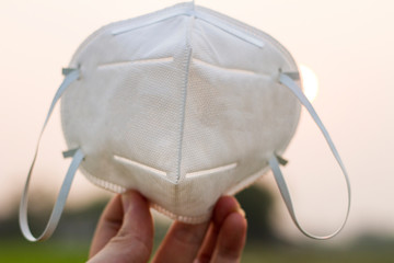 hand holding white n95 mask protect filter against air pollution (PM2.5) on sky background, wearing...