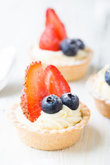 Cakes with fresh berries. Cream tartlet with strawberries and blueberries