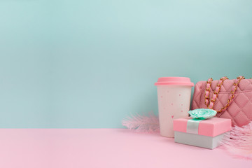 Fashion concept with bright colored accessories. Pink handbag, coffee cup and feathers