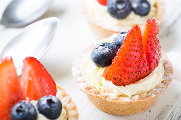 Cakes with fresh berries. Cream tartlet with strawberries and blueberries