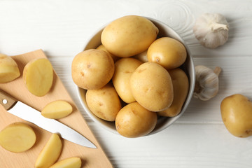 Bowl with young potato on wooden background, top view